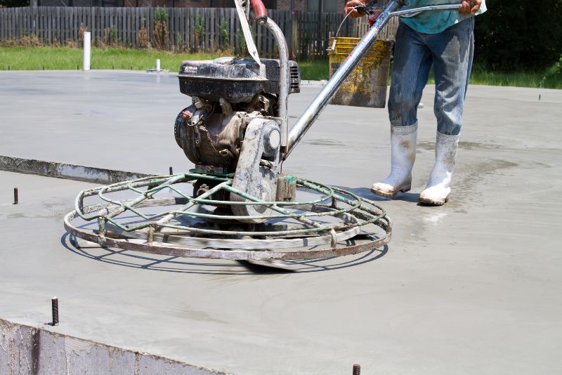 Concreter using a mechanical finishing tool to smooth a concrete surface